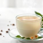 Friss, gőzölgő fehér tea egy átlátszó csészében, virágokkal és levelekkel díszítve.